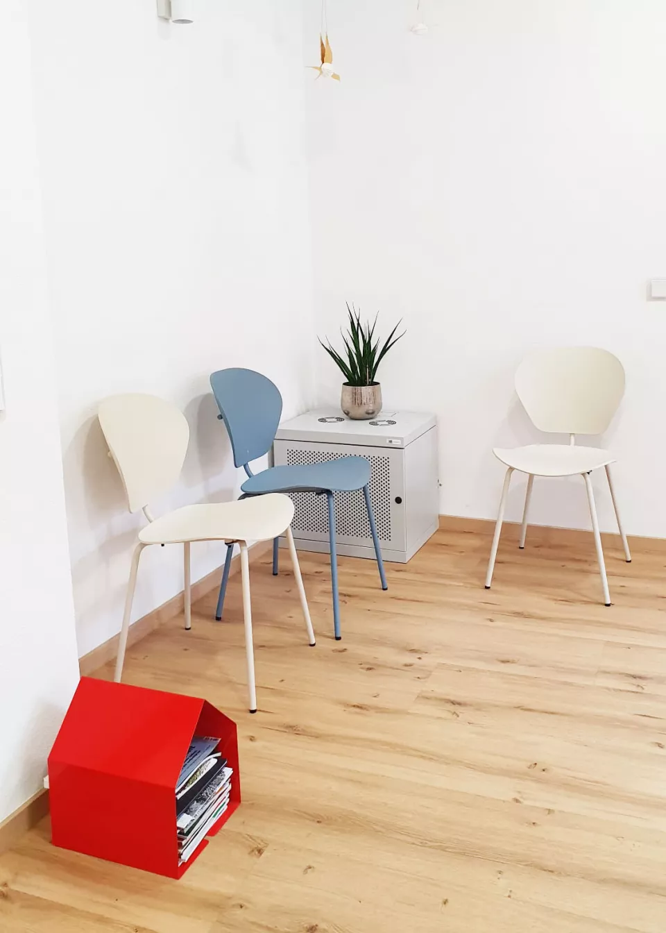 Heller und einladender Wartebereich der Praxis Seeger & Tändler mit farbenfrohen Stühlen, Zeitschriftenablage und Pflanze für eine angenehme Warteatmosphäre.