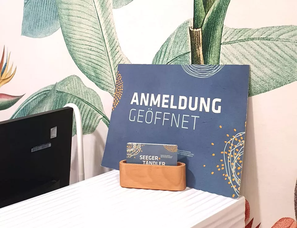 Ein Schild mit der Aufschrift „Anmeldung GEÖFFNET“ und Visitenkarte der Praxis Seeger & Tändler an der Anmeldung in Bischofswerda.